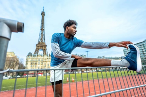 Young athletic man performing stretching exercises on a running track with the iconic eiffel tower