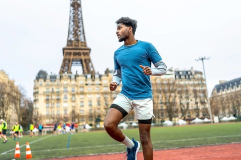 Young black man sprinting and training on an outdoor stadium track with the eiffel tower and