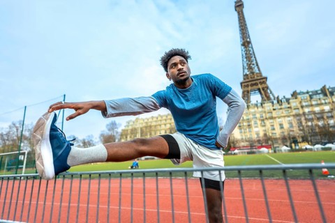 Young black man stretching legs on a paris running track before a workout, eiffel tower and