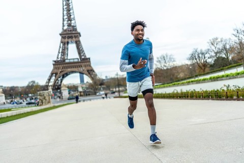 Athletic man jogging past the eiffel tower in paris, smiling and staying fit outdoors on a cloudy