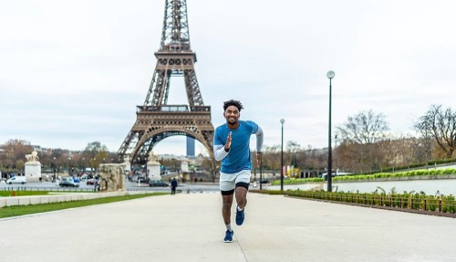 Young man actively running outdoors in front of the eiffel tower, symbolizing fitness, health, and
