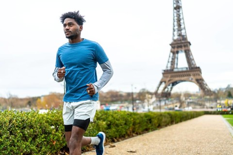 Young black man jogging along a path in a park with the eiffel tower in the background, focusing on