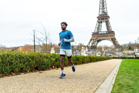 Young man actively jogging along a pathway in a parisian park, focusing on health and fitness with