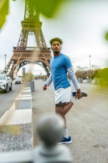 Young black man in sportswear stretching before a workout, standing on a sidewalk with the eiffel