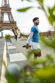 Young athletic man in sportswear stretching his quadriceps on a paris street with the eiffel tower
