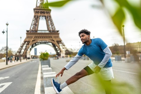 Fit young black man performing leg stretches in an urban environment with the eiffel tower in the
