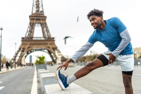 Young black man stretching leg on a concrete barrier with the eiffel tower in the blurred