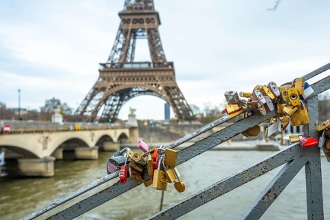 Many padlocks symbolizing everlasting love are attached to a bridge railing, with the iconic eiffel