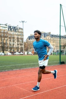Male athlete with dark skin running on an urban athletic track, training for endurance and