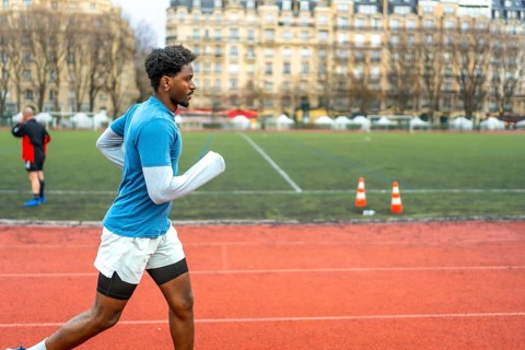 Sporty young black man running on an outdoor track in a stadium, focusing on fitness and urban