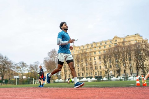 Young man training on a paris stadium running track, jogging in sportswear with focused