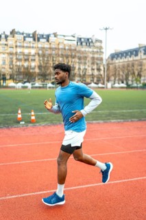 Young dark skinned athlete sprinting on a red urban track in paris, full body side view capturing