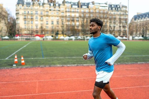 Young black man training on a running track with historic parisian buildings in the background,