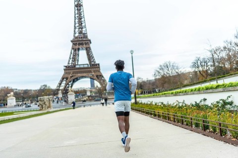 Young man in athletic wear jogging through a park pathway with the iconic eiffel tower prominently