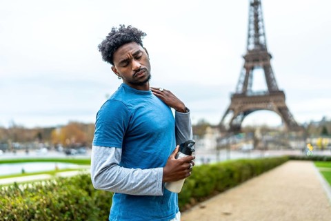 Young black athlete feeling neck pain and fatigue after exercising in a park, holding a water