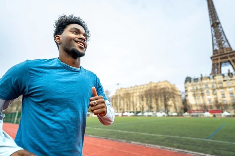 Young black man smiling and jogging outdoors on a running track with the iconic eiffel tower and