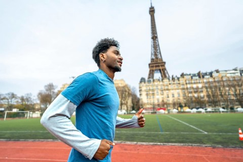 Young black man with curly hair running on a red athletic track in the city, the iconic eiffel