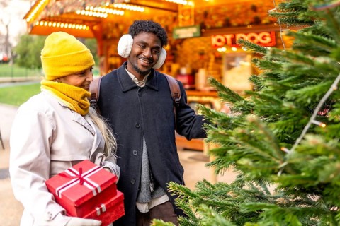 Joyful multiethnic couple holding red gifts, smiling as they stroll a festive paris christmas