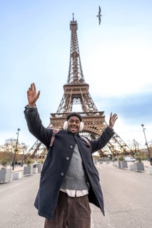 Young man with winter earmuffs raising arms in excitement and smiling widely while visiting the