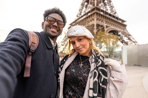 Diverse couple smiling for a close up selfie in front of the eiffel tower, embracing travel and