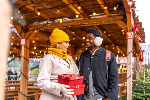 Young couple smiling at each other, walking and holding presents in red boxes at a festive outdoor