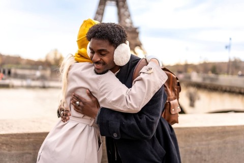 Diverse couple embracing outdoors in paris, smiling with joy and affection as they celebrate travel