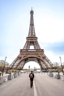 Solo traveler with backpack walks down a paris street toward the iconic eiffel tower, contemplating