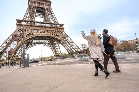 Happy couple holding hands and pointing toward the iconic eiffel tower while walking paris streets