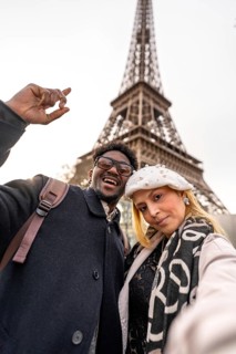 Diverse couple smiling for a selfie with the eiffel tower in the background, enjoying a romantic