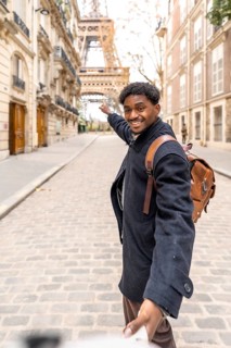 Happy black man leading someone by the hand down a cobblestone paris street, smiling and pointing