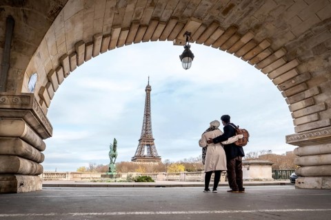 Couple stands embraced on pont de bir hakeim, framed by an ancient archway, observing the eiffel