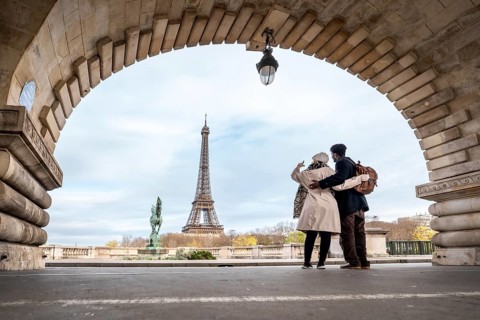 Loving couple embraces under an arched bridge in paris, taking a selfie with the eiffel tower in