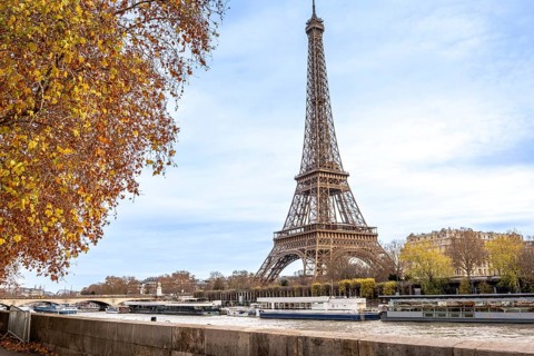 Eiffel tower rising beside the seine as tour boats glide past golden autumn trees and classic