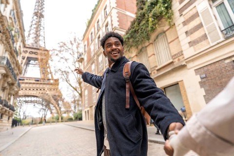 Happy young man of african descent leads his partner by the hand, pointing toward the eiffel tower