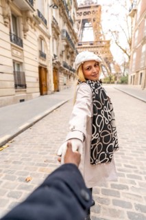 Woman holding her partner's hand, smiling and looking back while walking on a cobblestone paris