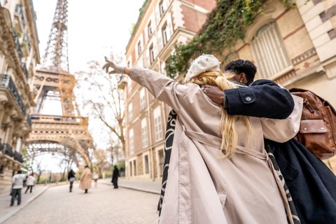 Young diverse couple embracing on a parisian street, with the woman pointing towards the distant
