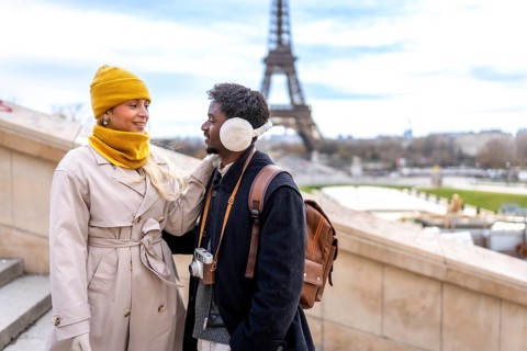 Diverse couple standing together with the eiffel tower in the background, enjoying their romantic