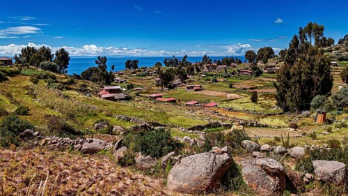 Hilly landscape with fields and huts near a blue lake, The countryside and farmhouses on Taquile