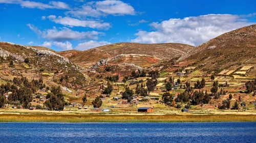 Wide landscape with hills, a lake and small villages, under a blue sky full of clouds, The