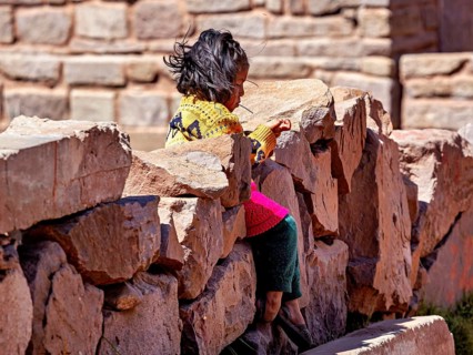 Little girl in colorful dress sitting on a stone wall and smiling, children from Taquile Island in