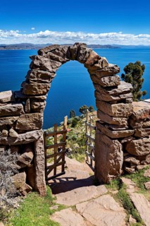 Stone archway with wooden gate in peaceful surroundings, with a view of vast blue lake and sky,