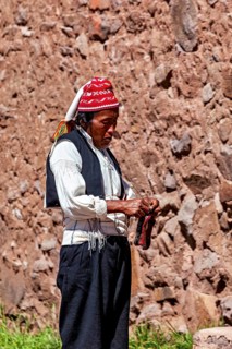 Close-up of a man wearing a red cap and traditional clothes on a stone wall, The knitting men on