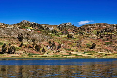 Wide fields stretch across rolling hills overlooking a lake, countryside and farmhouses on Taquile