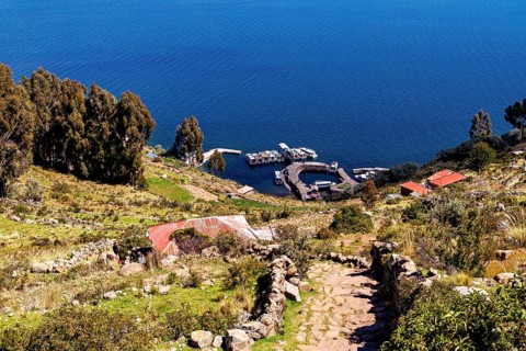 Trail leads to boats on the shores of a deep blue lake surrounded by vegetation, countryside and