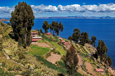 Cabins on terraces with trees and views of blue lake under clear skies, countryside and farmhouses