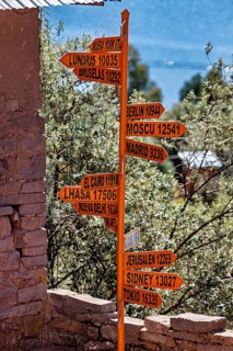 An orange signpost with several international cities and distances in front of a stone wall in a