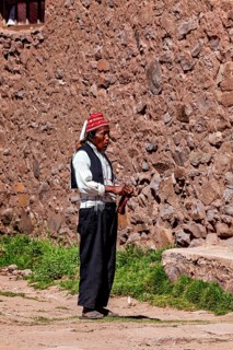 Elderly man wearing traditional clothes next to a stone wall under clear skies, The knitting men on