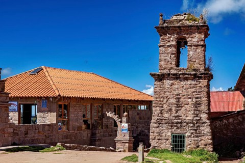 A historic stone building with a bell tower and red tile roofs against a blue sky, The historic