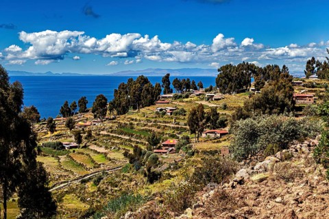 A terraced village stretches along a hill overlooking a blue lake, countryside and farmhouses on