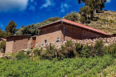 Two people in front of rustic farm houses surrounded by green fields under a blue sky, the